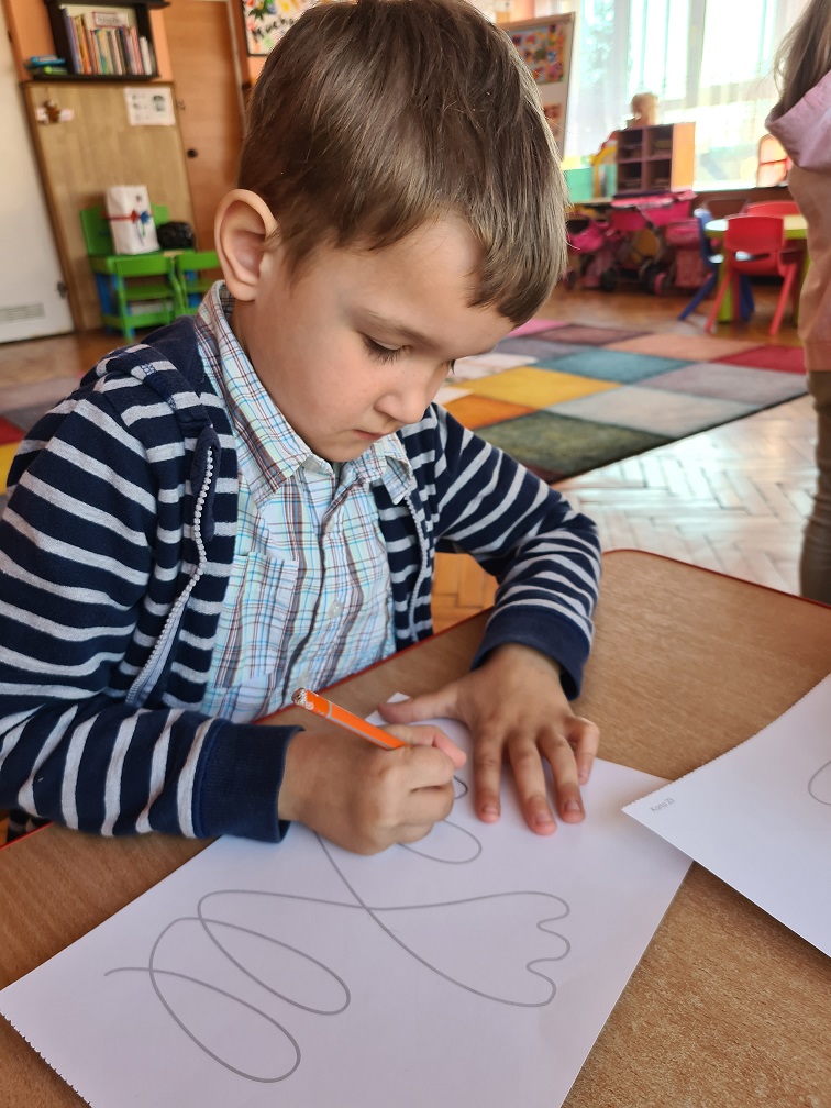 Chłopiec przy stoliku rysuje ołówkiem po śladzie.