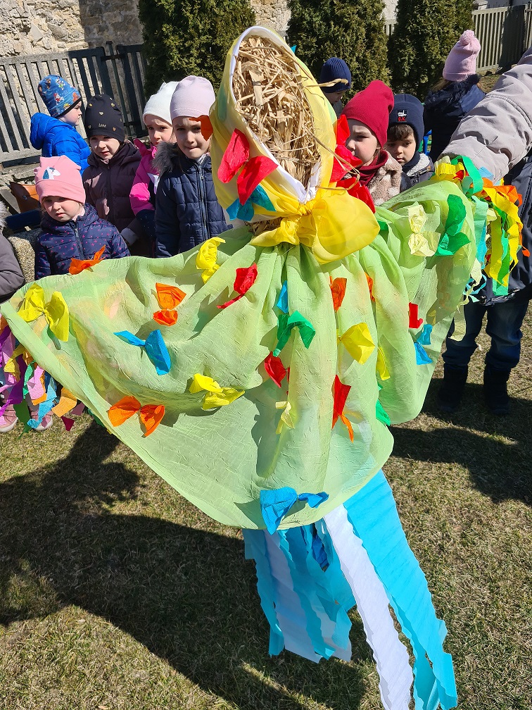 Dzieci zakładają kukle Marzanny piękną zieloną , ozdobioną kolorowymi kokardkami chustkę i pelerynę.