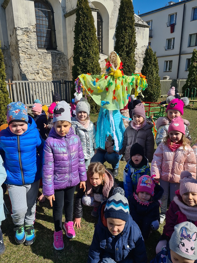 Dzieci z grupy Muchomorków entuzjastycznie witają Panią Wiosnę. Stoją blisko przebranej kukły.