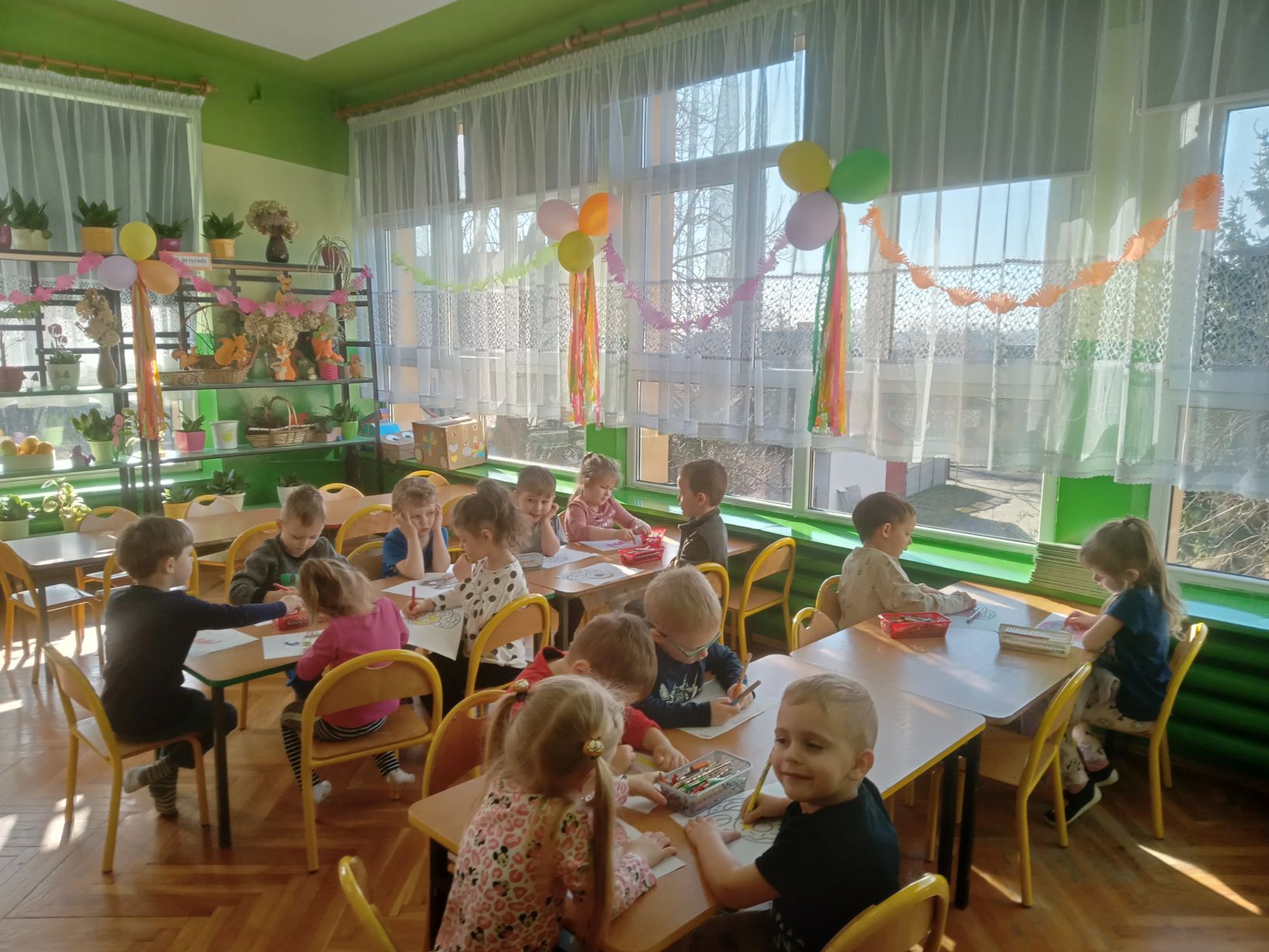 dzieci siedzą przy stolikach i kolorują obrazek pączka