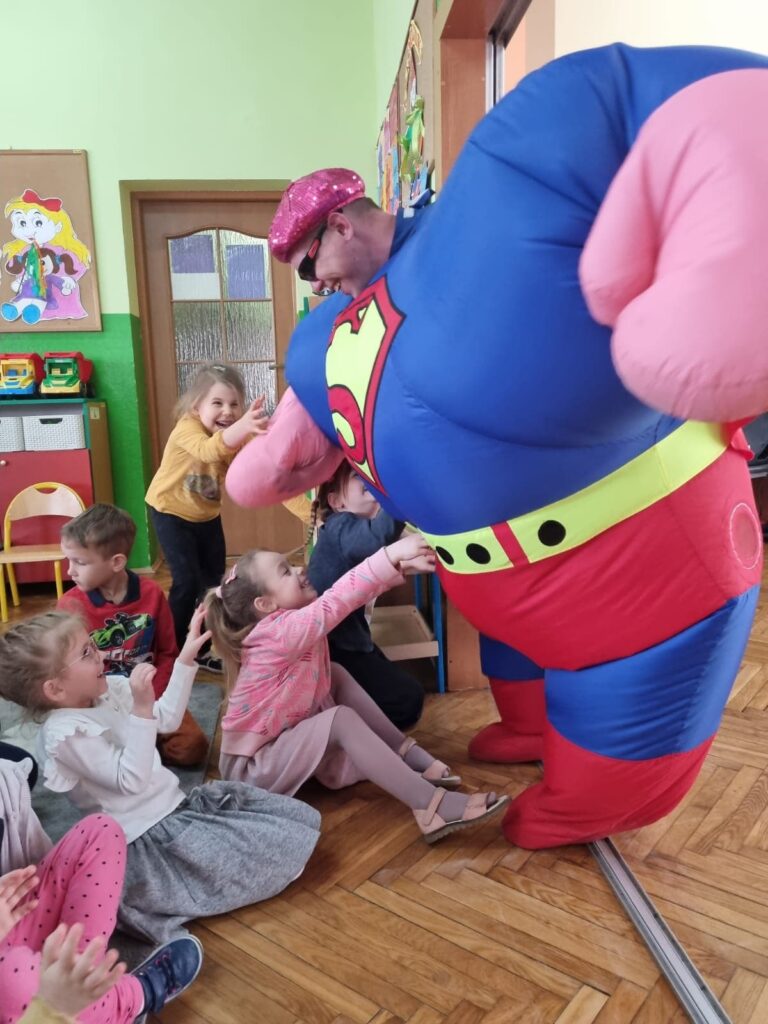 Ogromny Superman wita się z przedszkolakami.