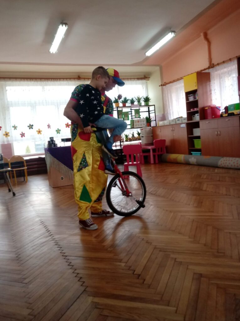 Klaun uczy chłopca jeździć na rowerku cyrkowym.