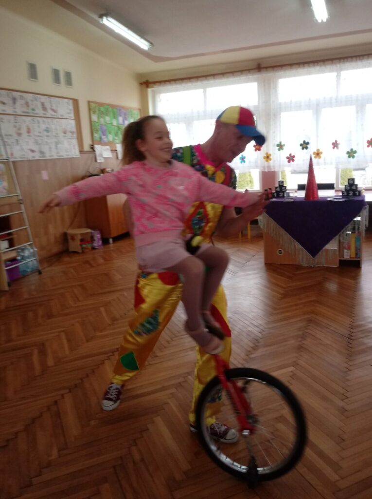 Klaun uczy dziewczynkę jeździć na rowerku cyrkowym.