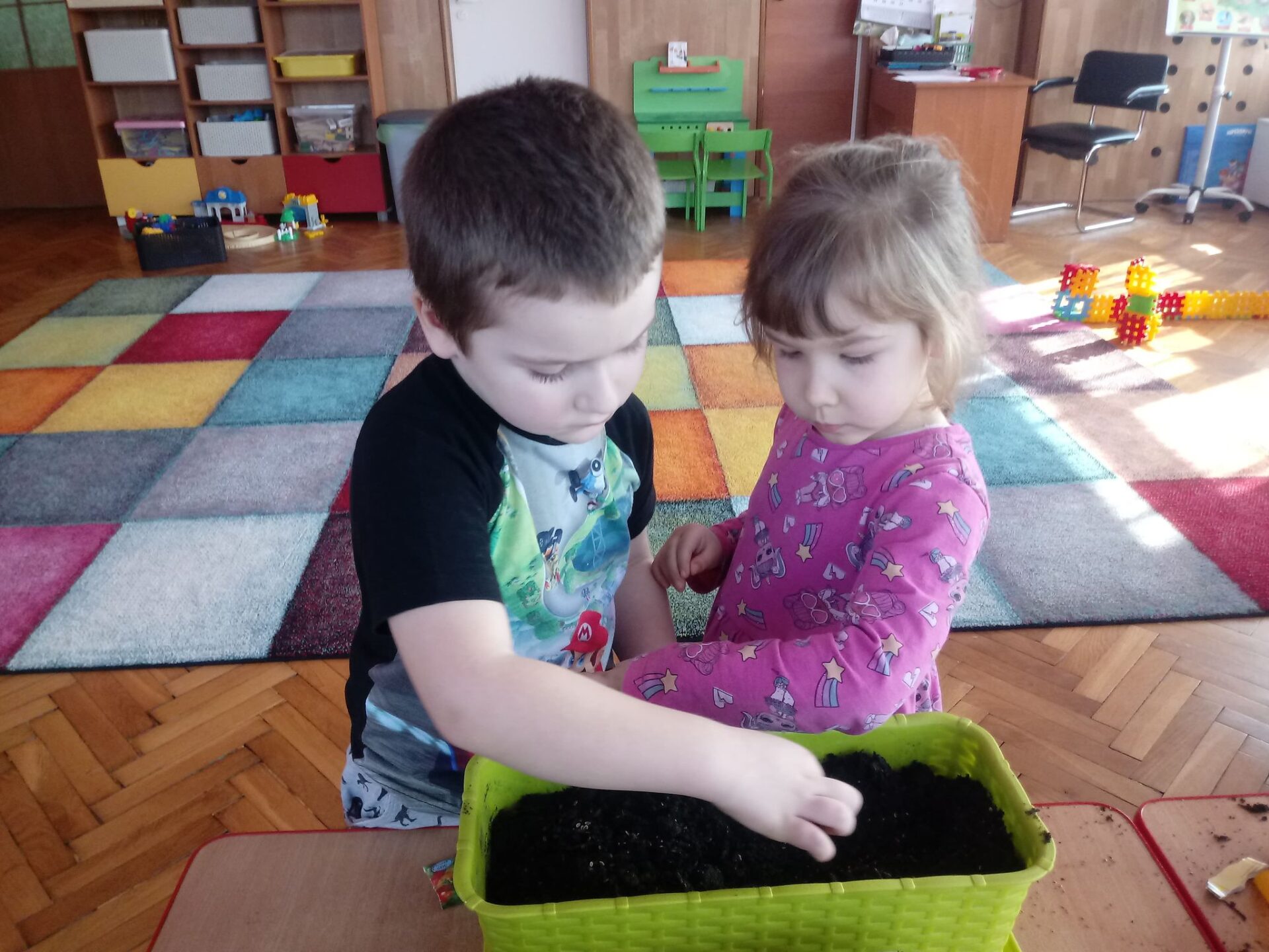 Dziewczynka i chłopiec sadzą cebulki w doniczce