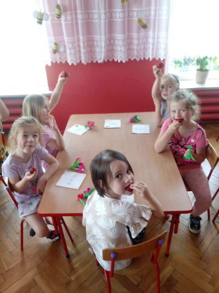 Dziewczynki przy stoliku jedzą truskawki