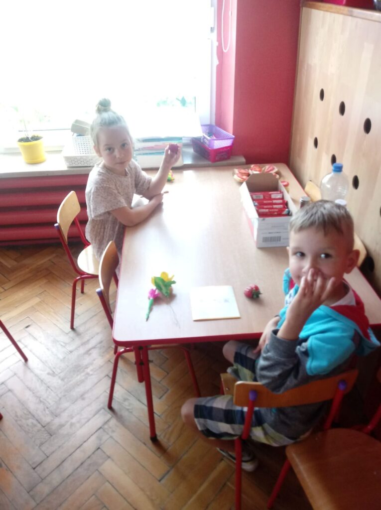 Dzieci przy stoliku jedzą truskawki