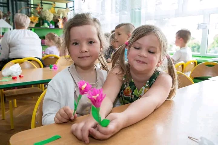 Dwie dziewczynki pokazują samodzielnie wykonane ludowe kwiatki