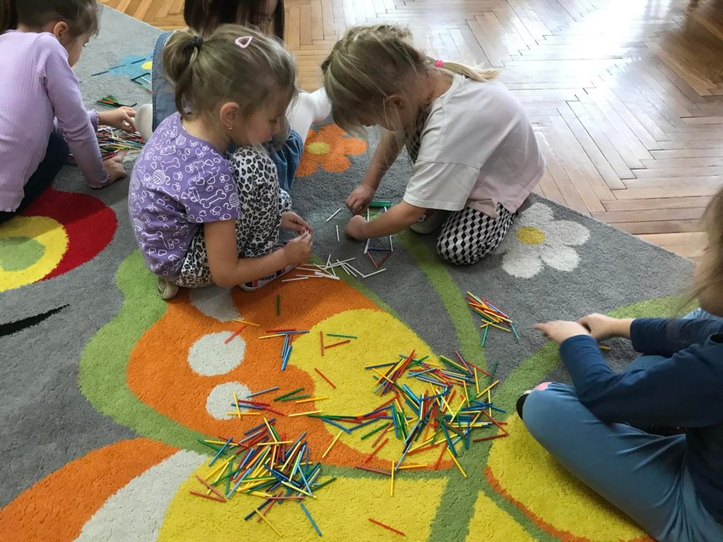 Dziewczynki układają obrazki z kolorowych patyczków.