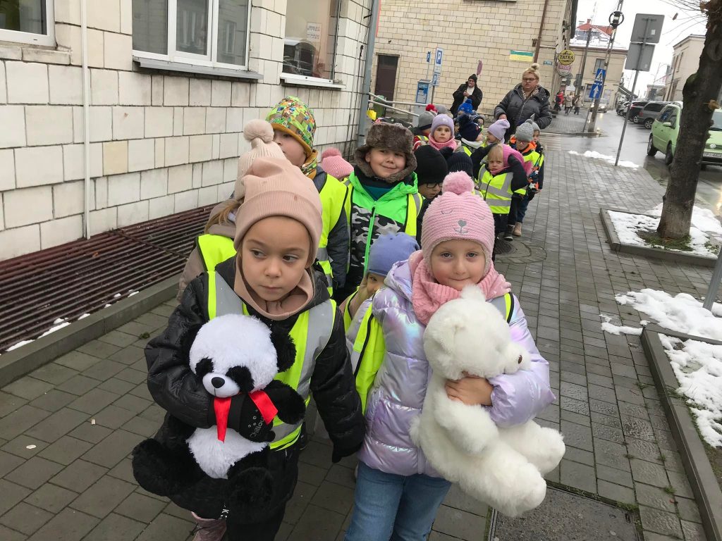 Dzieci idą chodnikiem z misiami w rękach.