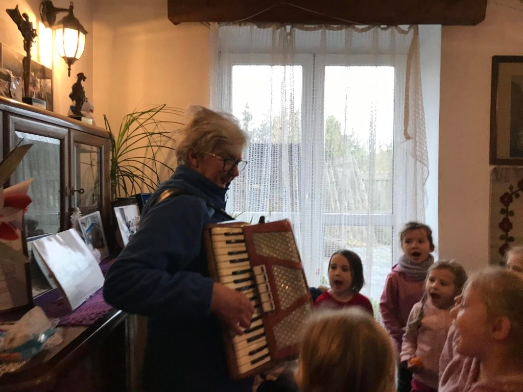 Dzieci słuchają gry na akordeonie i śpiewają.