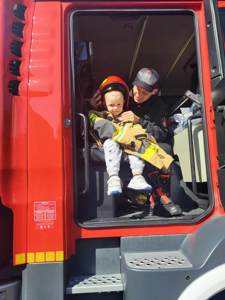 Chłopiec w hełmie strażackim siedzi w wozie strażackim