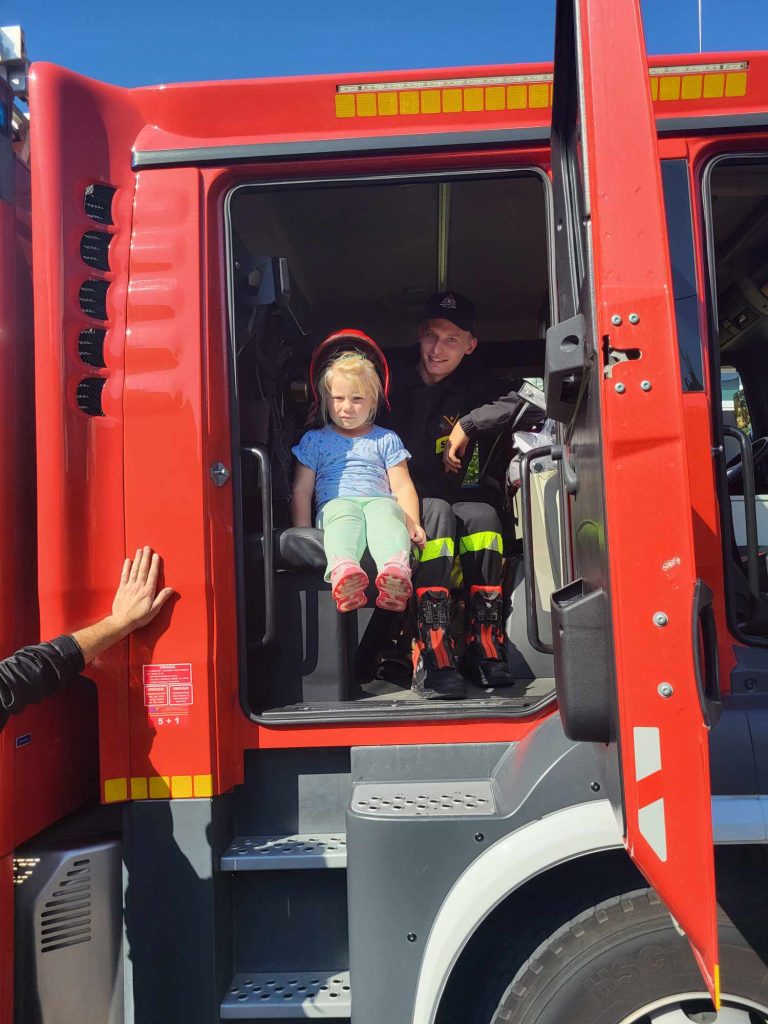 Dziewczynka w hełmie strażackim siedzi w wozie strażackim