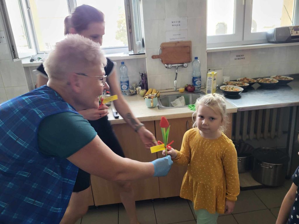Dzieci składają życzenia pracownikom i wręczają kwiatuszki