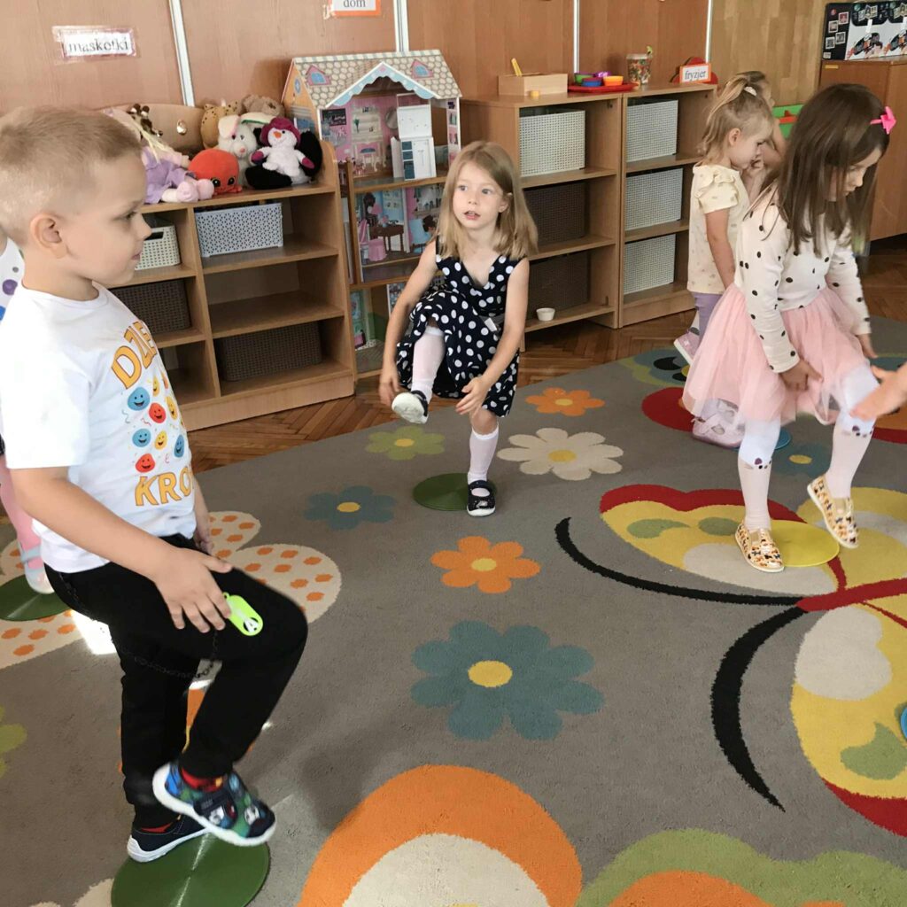 Dzieci stoją na kolorowych kropkach wyciętych z papieru.