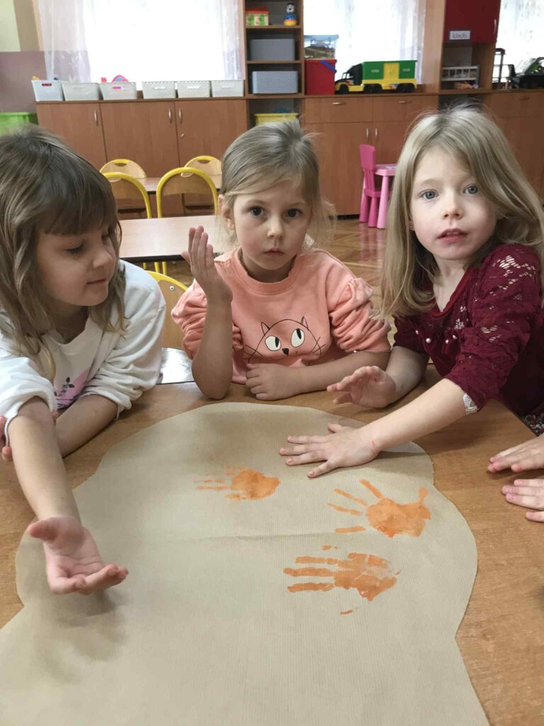 Dzieci obijają odcisk dłoni na kartonie.