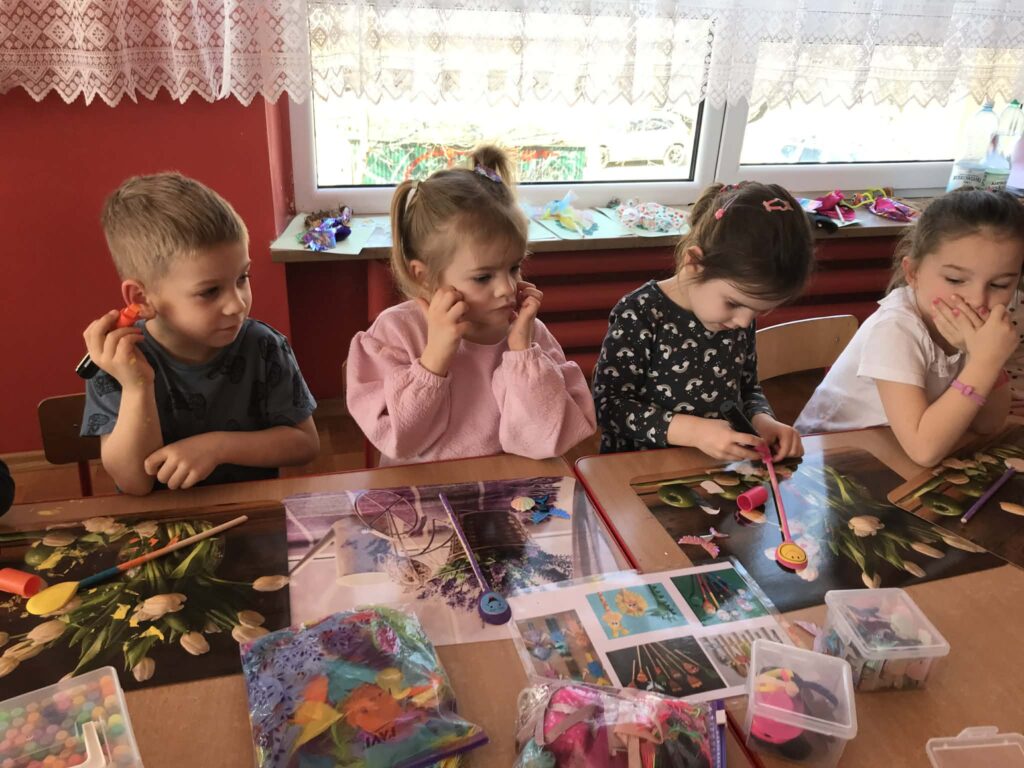 Dzieci tworzą przy stolikach własne kukiełki.