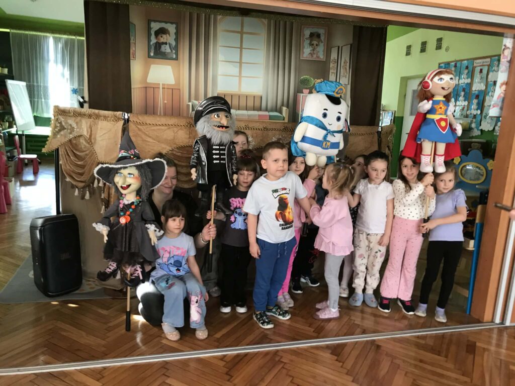 Dzieci stoją na tle scenografii z kukiełkami.