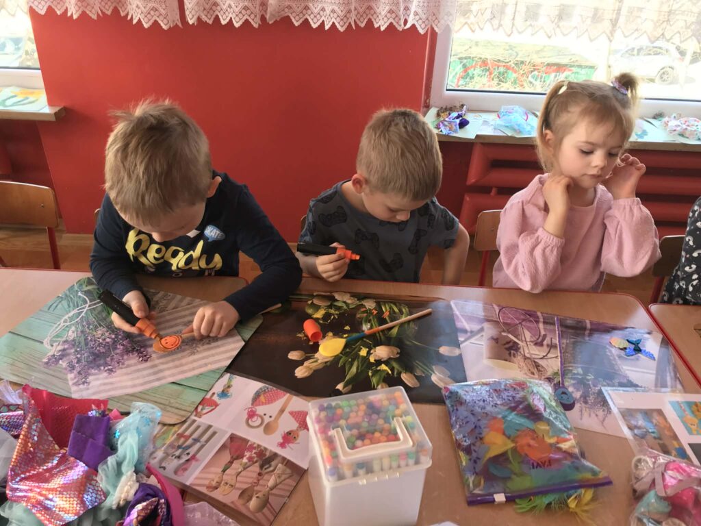 Dzieci tworzą przy stolikach własne kukiełki.